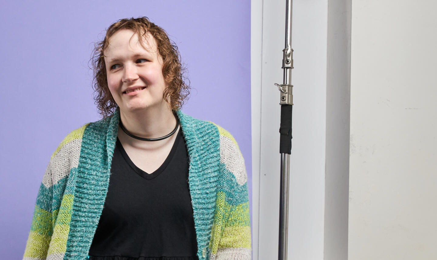 Triana wearing a broadcast headset on a stage with colourful purple and pink lights behind her. A logo for the mental health charity ReachOut is on a giant screen.
